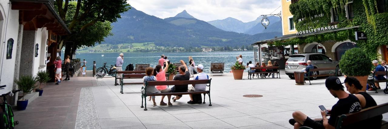Der Schiffsanlegeplatz in St. Wolfgang am Wolfgangsee. Mehrere Menschen sitzen auf Bänken oder gehen durch die Fußgängerzone am Seeufer. Der Schiffsanlegeplatz in St. Wolfgang am Wolfgangsee. Mehrere Menschen sitzen auf Bänken oder gehen durch die Fußgängerzone am Seeufer.