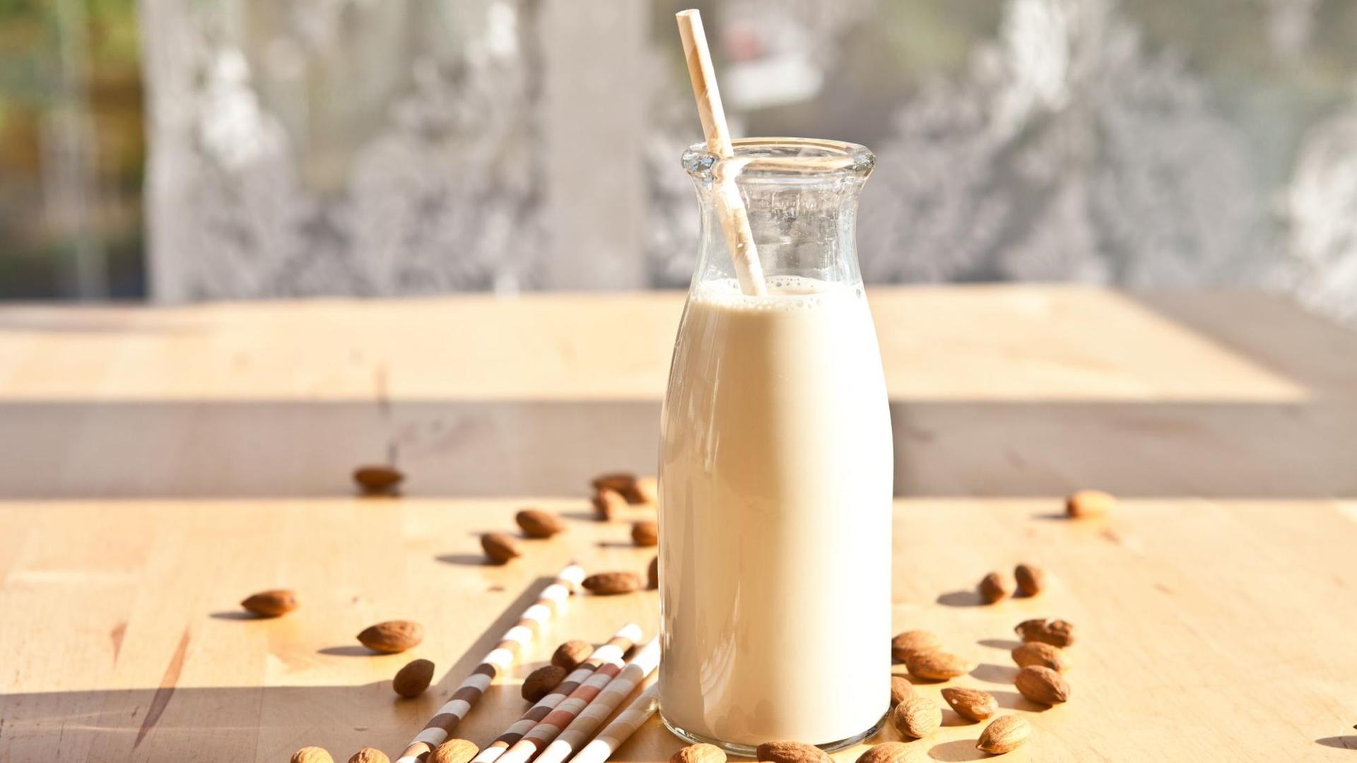 Eine Mandelmilch in Vintage-Milchflasche steht auf einem Tisch mit Trinkhalmen und Mandeln Eine Mandelmilch in Vintage-Milchflasche steht auf einem Tisch mit Trinkhalmen und Mandeln