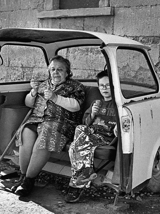 Grossmutter und Enkel essen Eis in einem als Sitzbank hergerichteten ausrangierten Trabant.