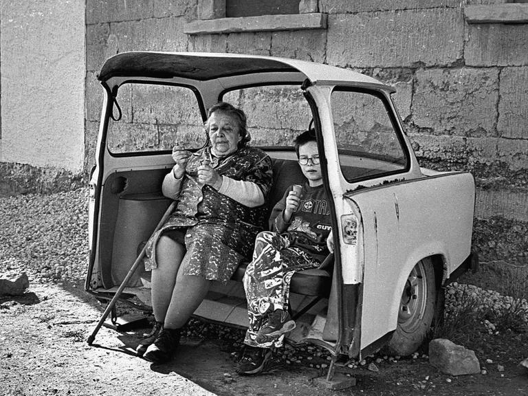 Grossmutter und Enkel essen Eis in einem als Sitzbank hergerichteten ausrangierten Trabant.