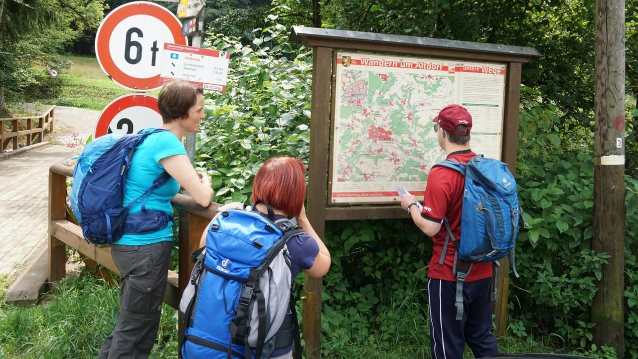 Eine Wandergruppe schaut sich Informationstafel mit einer Karte an. Eine Wandergruppe schaut sich Informationstafel mit einer Karte an.