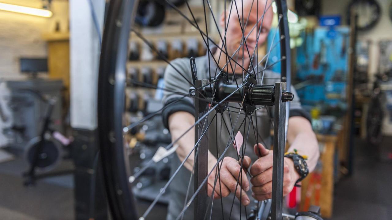 Ein Fahrradmechaniker der ein eingespanntes Vorderrad prüft. Ein Fahrradmechaniker der ein eingespanntes Vorderrad prüft.