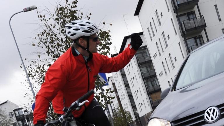 Ein Radfahrer hebt die Faust gegen ein ankommendes Auto. Ein Radfahrer hebt die Faust gegen ein ankommendes Auto.