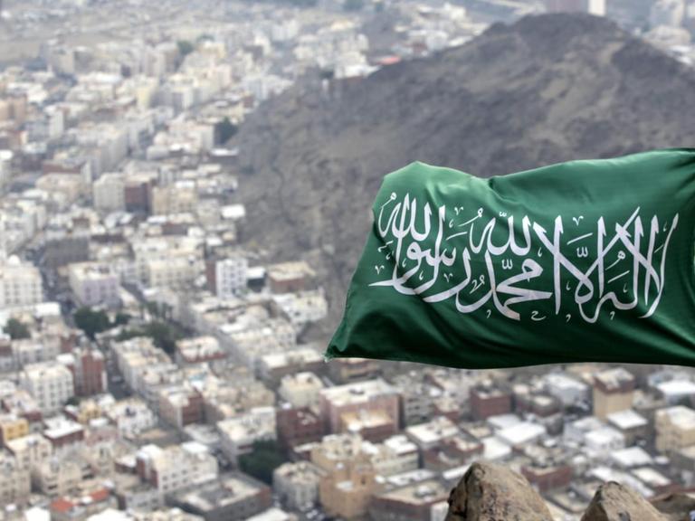 Eine saudi-arabische Fahne weht auf dem Berg Hira. Dahinter sind Häuser zu sehen.