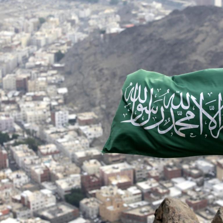 Eine saudi-arabische Fahne weht auf dem Berg Hira. Dahinter sind Häuser zu sehen.