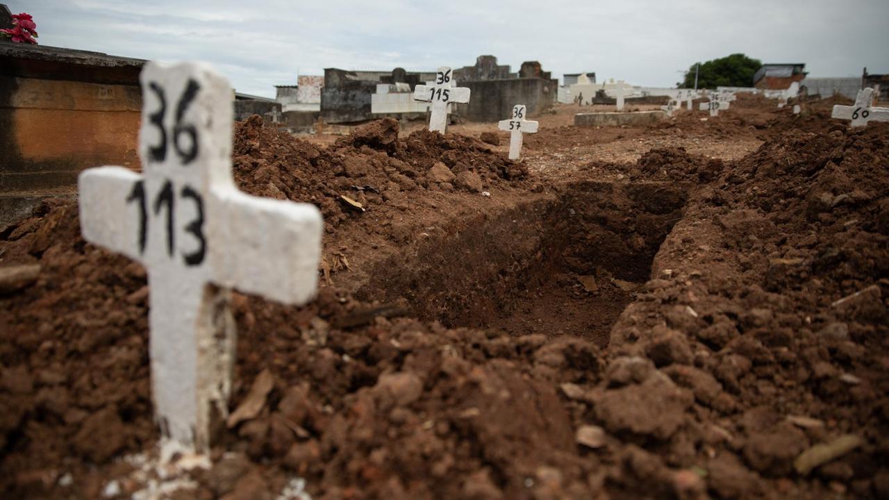 Ein einfaches Kreuz ohne Namen und mit einer Nummer steht an einem offenen Grab am Friedhof von Iraja. Ursprünglich für die Armen vorgesehen, sind die Gräber ohne Namen in der Corona-Pandemie zu eine der wenigen erschwinglichen Optionen für viele Familien geworden, Angehörige zu begraben. Ein einfaches Kreuz ohne Namen und mit einer Nummer steht an einem offenen Grab am Friedhof von Iraja. Ursprünglich für die Armen vorgesehen, sind die Gräber ohne Namen in der Corona-Pandemie zu eine der wenigen erschwinglichen Optionen für viele Familien geworden, Angehörige zu begraben.