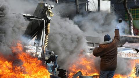 Ein Demonstrant wirft einen Pflasterstein, im Hintergrund brennt ein Auto.