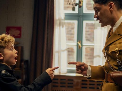 Szene aus dem Film "Jojo Rabbit": Ein Junge und ein Mann in der Verkleidung Hitlers zeigen mit Fingern aufeinander.