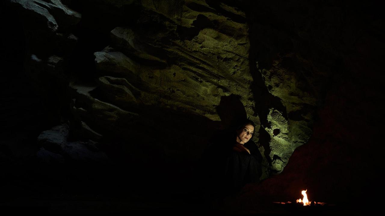Dalila in einer dunklen, nur vom Lichtschein eines kleinen Feuers erhellten Höhle.