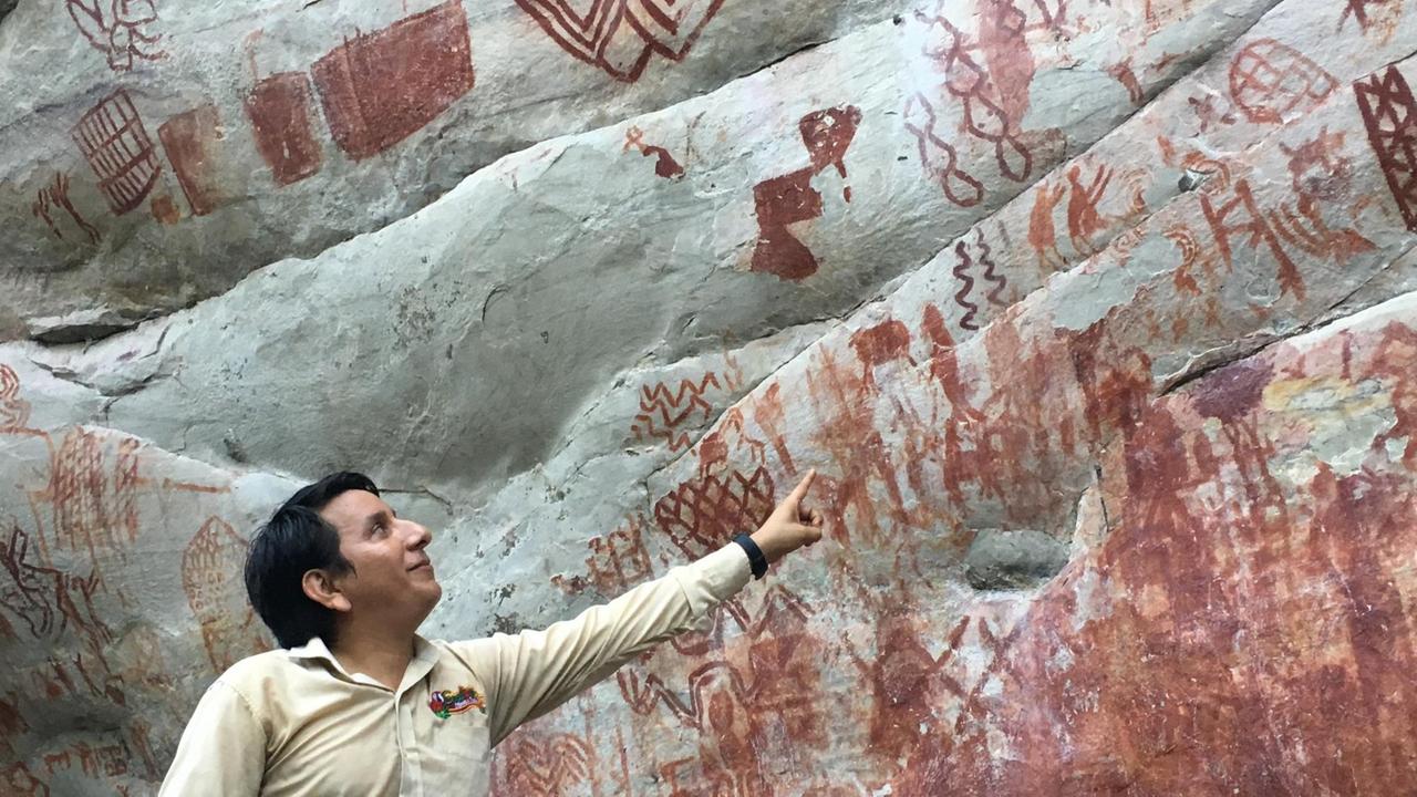 Ein junger Mann zeigt auf Steine, auf denen rote Malereien zu sehen sind.