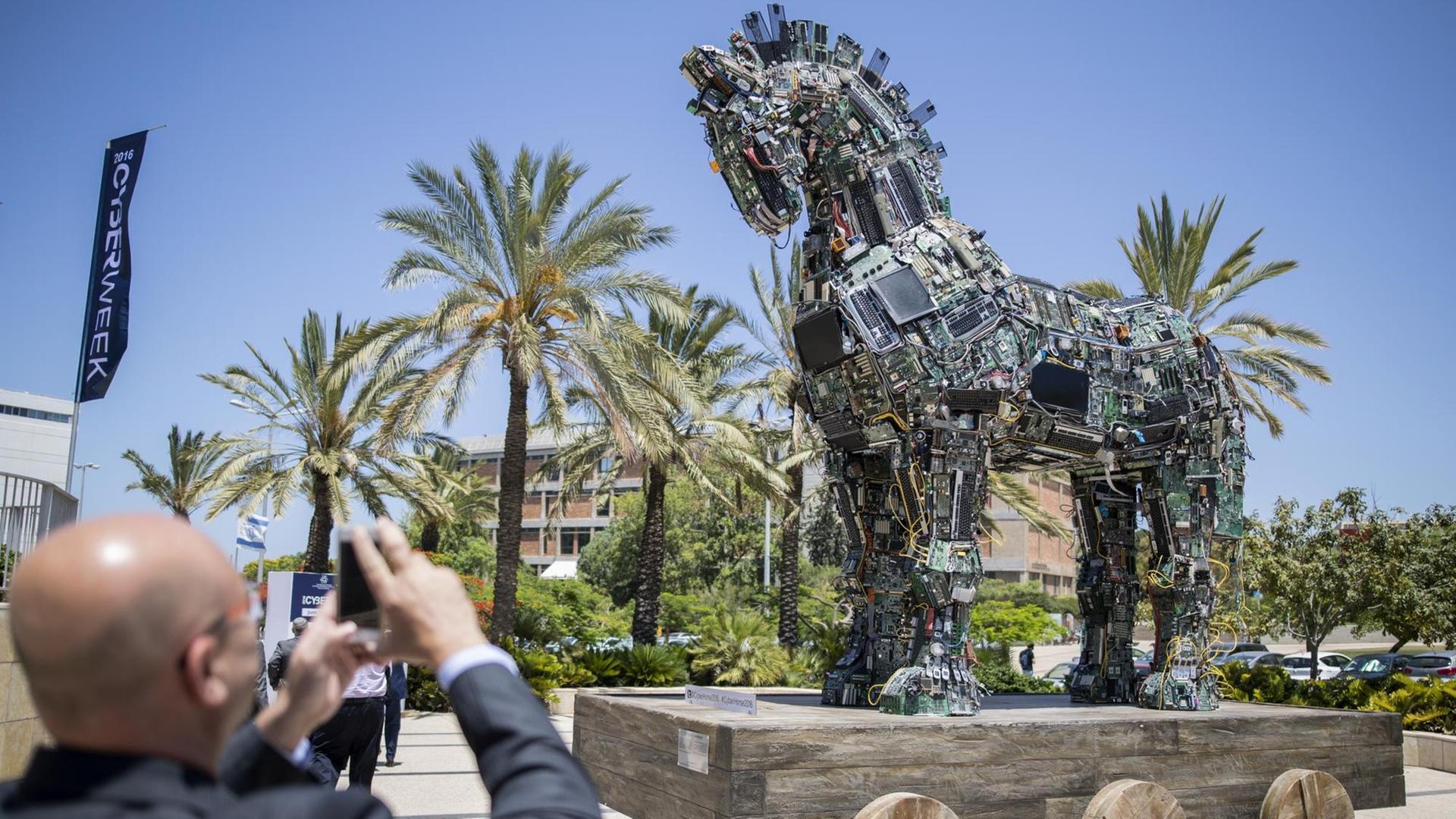 Ein Mann fotografiert die Skulptur eines Trojanischen Pferdes, zusammengesetzt aus mit Malware infizierten Computerteilen. Ein Mann fotografiert die Skulptur eines Trojanischen Pferdes, zusammengesetzt aus mit Malware infizierten Computerteilen.