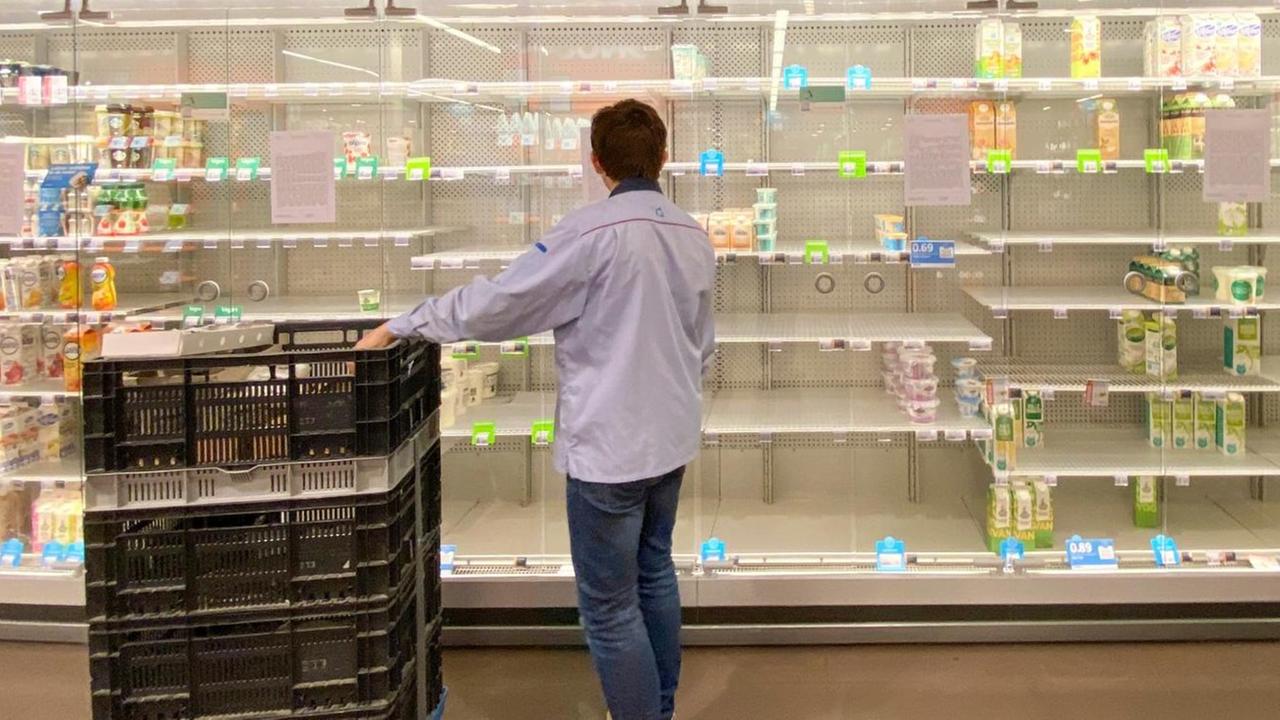 Ein junger Mann räumt ein halbleeres Supermarktregal ein. Ein junger Mann räumt ein halbleeres Supermarktregal ein.