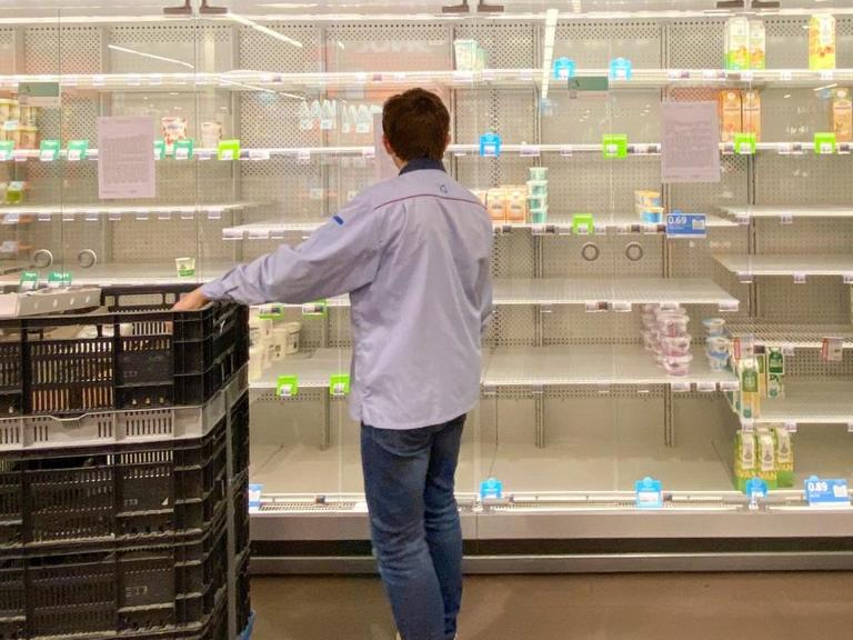 Ein junger Mann räumt ein halbleeres Supermarktregal ein.