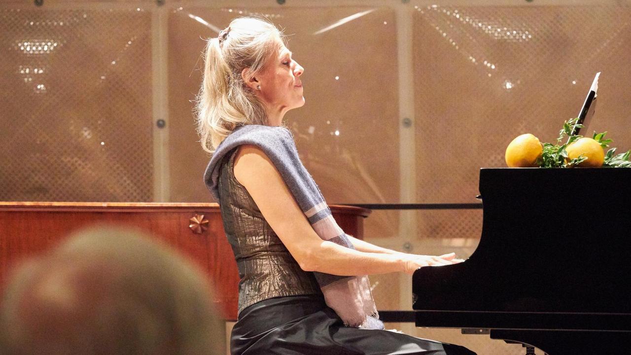 Die Pianistin spielt mit geschlossenen Augen auf dem Klavier, darauf liegen Orangen und Myrthen Die Pianistin spielt mit geschlossenen Augen auf dem Klavier, darauf liegen Orangen und Myrthen