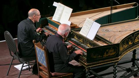 An zwei Cembali, die nebeneinander stehen, sitzen die beiden Musiker.