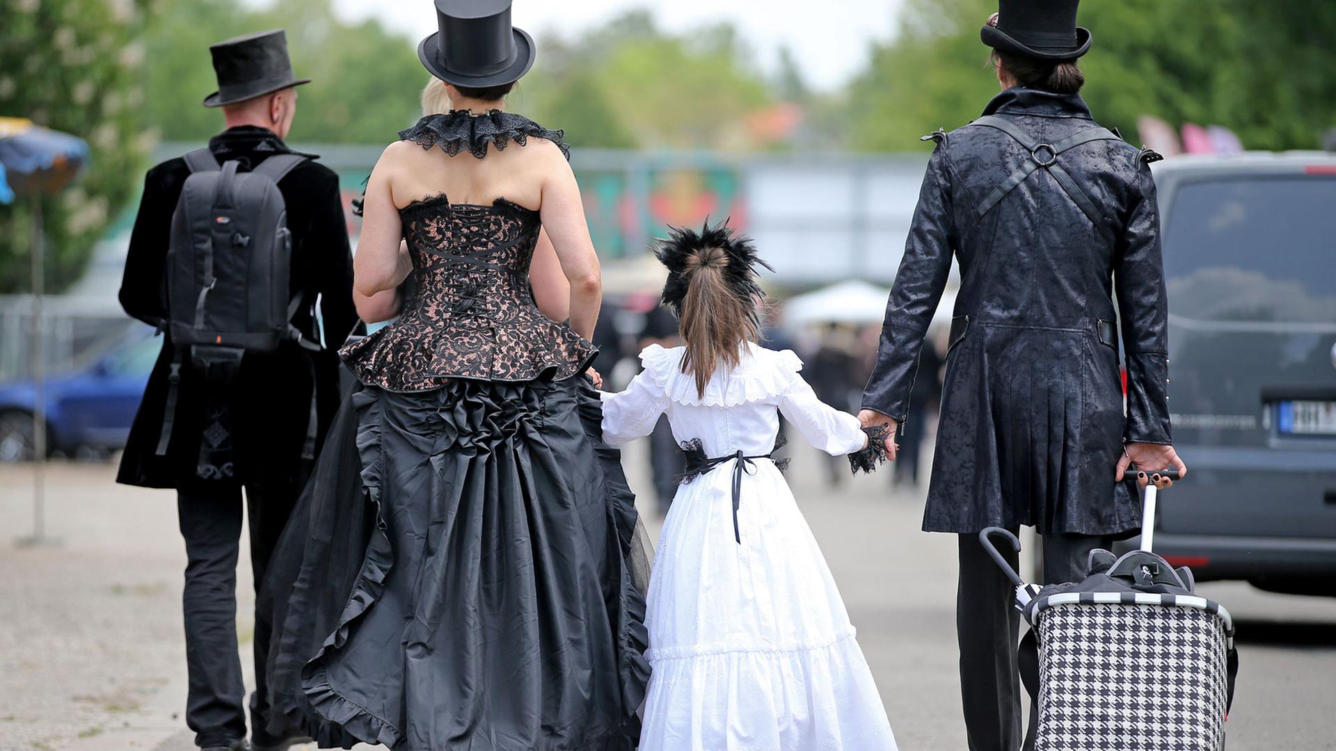 Besucher des Wave Gotik Treffens (WGT) gehen mit einem kleinen Mädchen an der Hand über das Veranstaltungsgelände agra in Leipzig.