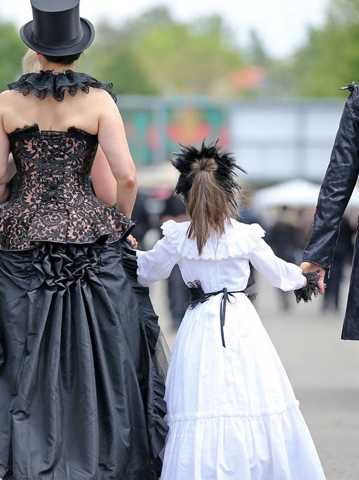 Besucher des Wave Gotik Treffens (WGT) gehen mit einem kleinen Mädchen an der Hand über das Veranstaltungsgelände agra in Leipzig.