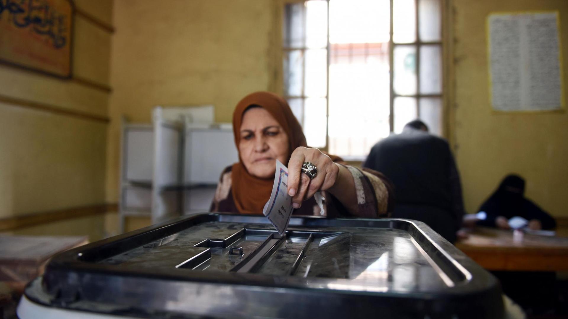 Eine Frau steckt ihren Wahlzettel für die Parlamentswahl in Ägypten in eine Wahlurne.