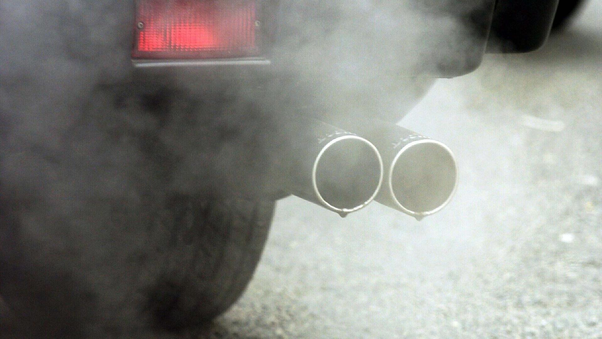 Aus dem Auspuff von einem Auto kommt eine Abgas-Wolke. Aus dem Auspuff von einem Auto kommt eine Abgas-Wolke.
