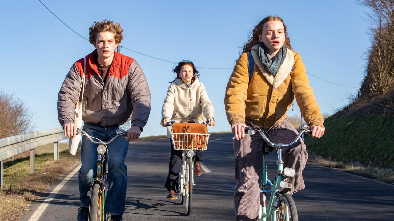 Drei Jugendliche fahren auf ihren Fahrädern gemeinsam eine Straße hintunter.