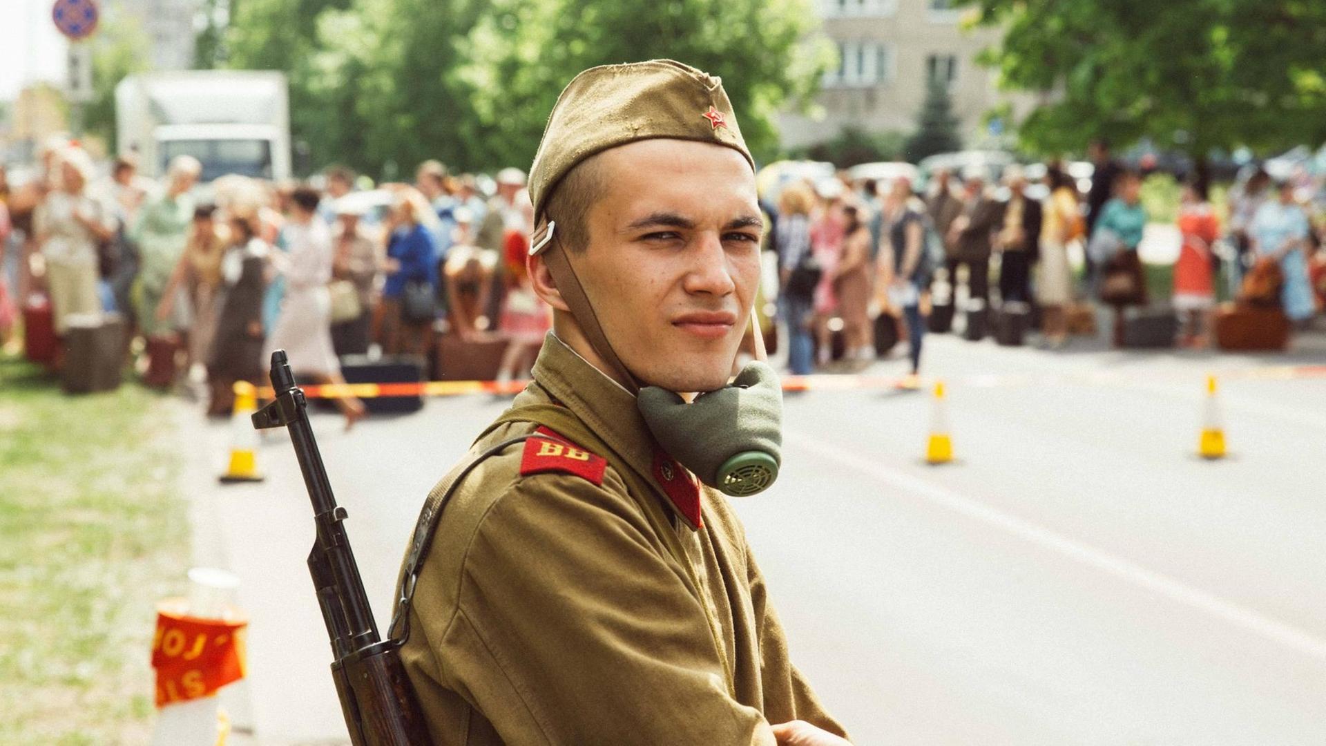 Ein Soldat mit einer Atemschutzmaske um den Hals schaut in die Kamera. Im Hintergrund, in der Unschärfe viele Statisten. Ein Soldat mit einer Atemschutzmaske um den Hals schaut in die Kamera. Im Hintergrund, in der Unschärfe viele Statisten.