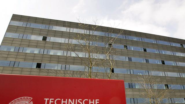 Rotes Schild mit der Aufschrift "Technische Universität Darmstadt" vor einem großen Gebäude.