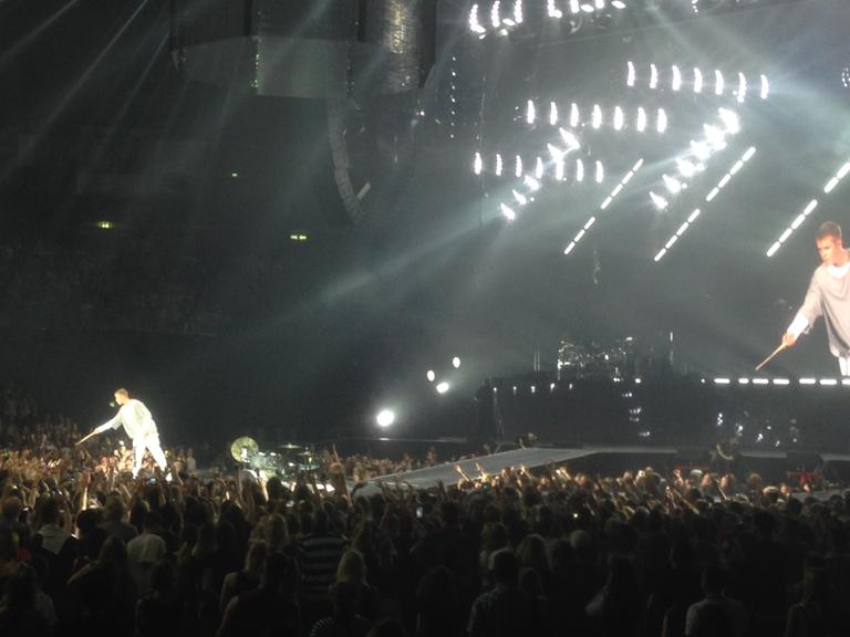Der kanadische Musiker Justin Bieber steht bei einem Auftritt in Berlin am 14.09.2016 ganz in Weiß gekleidet auf der Bühne, dahinter ist er vergrößert auf einer Leinwand zu sehen.