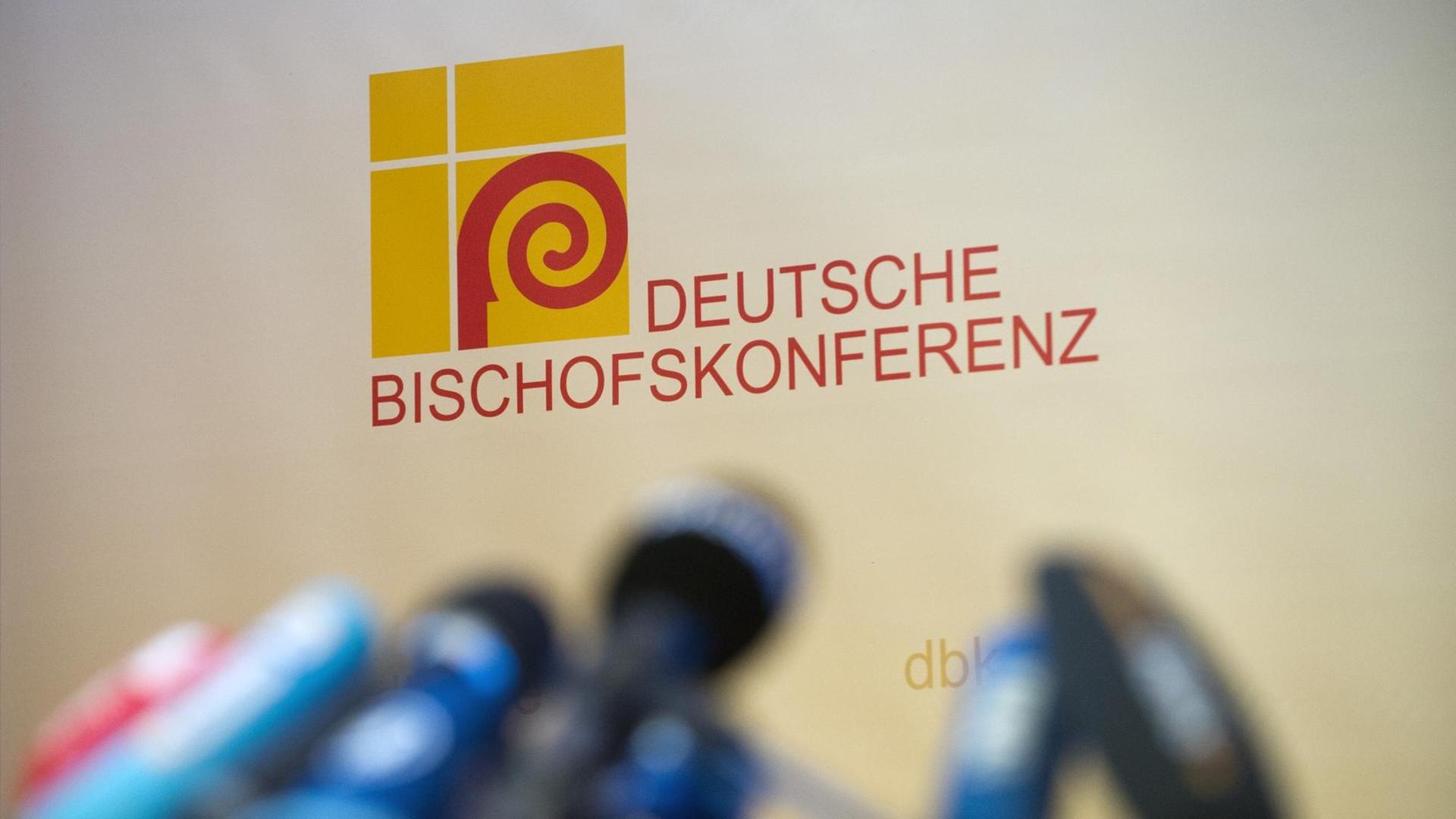 Presse-Mikrofone stehen unscharf abgelichtet vor dem Logo der Deutschen Bischofskonferenz