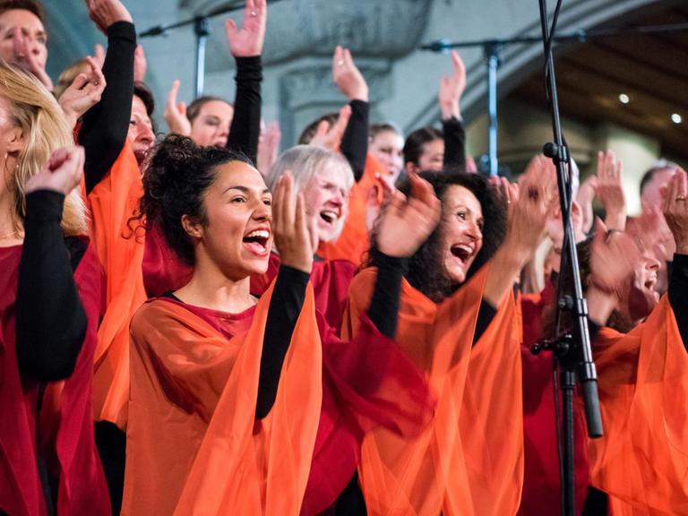 Sängerinnen des Chores bei einem Konzert. Sie singen, sie klatschen in die Hände und tanzen dazu.