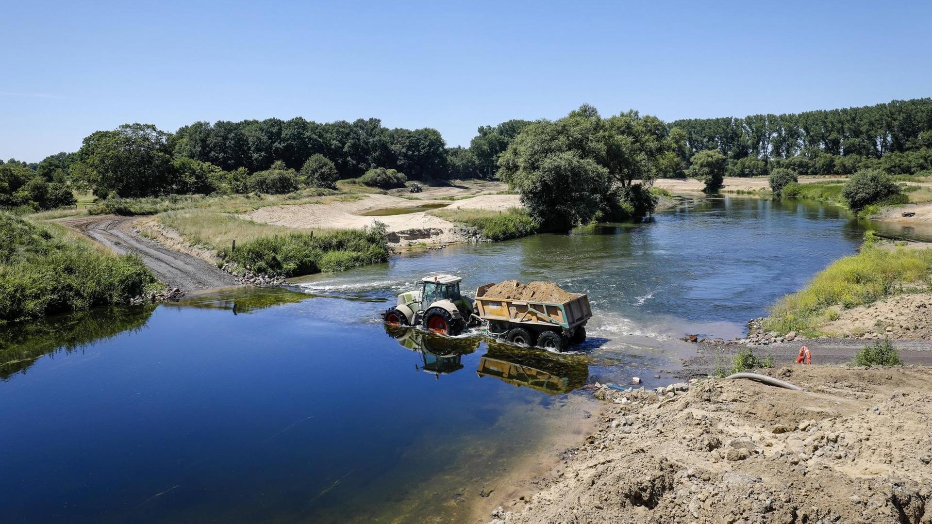 Ein Trecker mit einem Anhänger voller Sand durchquert den Fluss Lippe. Hier wird eine naturnahe Flusslandschaft geschaffen, ein intaktes Fluss-Auen-Ökosystem wiederhergestellt. Ein Trecker mit einem Anhänger voller Sand durchquert den Fluss Lippe. Hier wird eine naturnahe Flusslandschaft geschaffen, ein intaktes Fluss-Auen-Ökosystem wiederhergestellt.