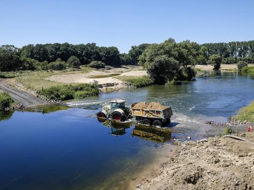 Ein Trecker mit einem Anhänger voller Sand durchquert den Fluss Lippe. Hier wird eine naturnahe Flusslandschaft geschaffen, ein intaktes Fluss-Auen-Ökosystem wiederhergestellt.