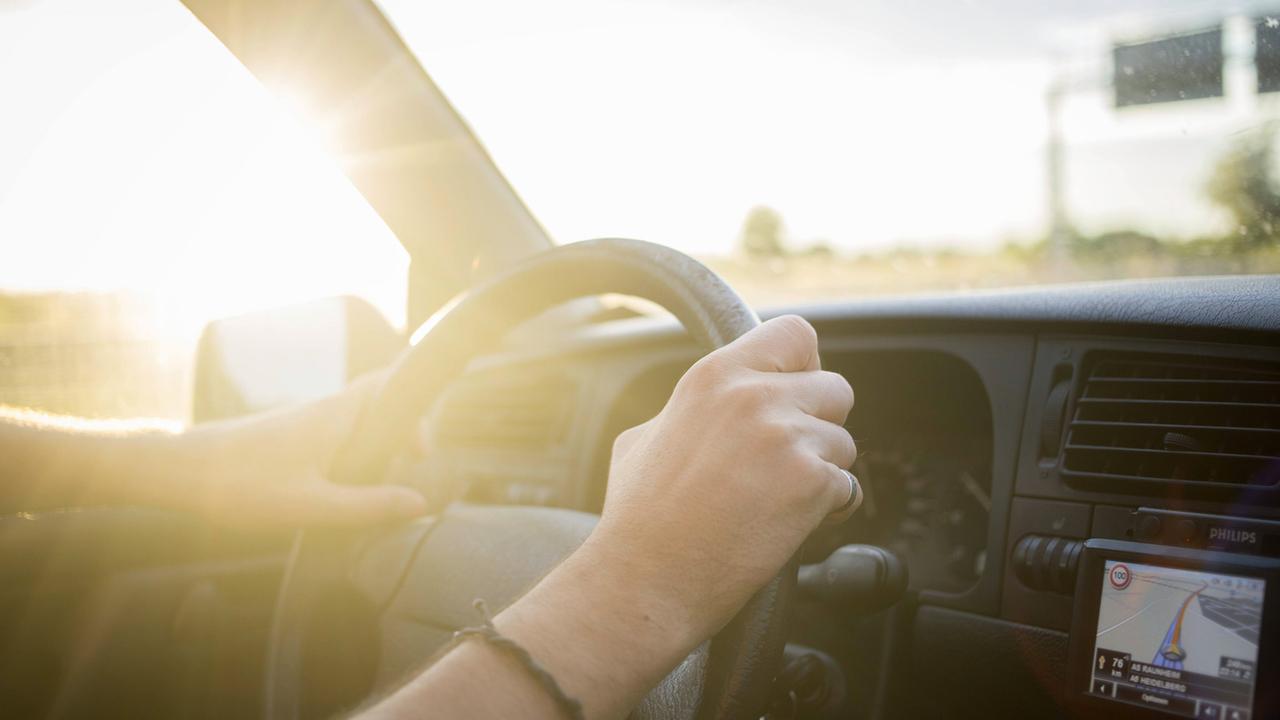Ein Mann sitzt bei untergehender Sonne am Steuer seines Autos. Ein Mann sitzt bei untergehender Sonne am Steuer seines Autos.