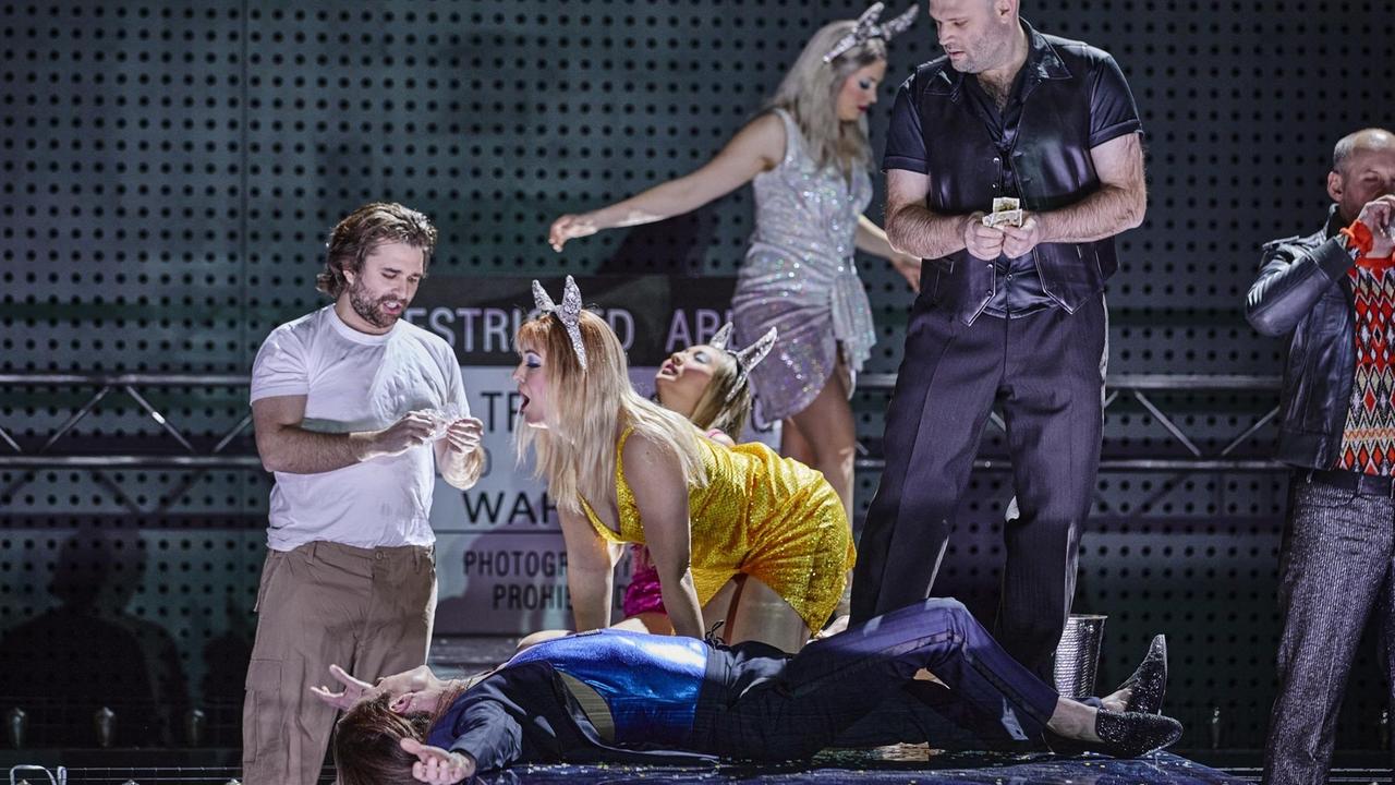 Szenenfoto: Im Bild sind vier Männer und drei Frauen zu sehen. Die Frauen tragen Haarreifen mit Glitzer-Hasenohren. Ein Mann liegt auf dem Boden mit ausgestreckten Armen. Ein Mann steht mitten im Bild, zählt Geldscheine und trägt ebenfalls einen solchen Haarreifen. Eine Frau kniet mit offenem Mund, ein ihr gegenüber stehender Mann fummelt etwas aus einer kleinen Plastiktüte heraus. Szenenfoto: Im Bild sind vier Männer und drei Frauen zu sehen. Die Frauen tragen Haarreifen mit Glitzer-Hasenohren. Ein Mann liegt auf dem Boden mit ausgestreckten Armen. Ein Mann steht mitten im Bild, zählt Geldscheine und trägt ebenfalls einen solchen Haarreifen. Eine Frau kniet mit offenem Mund, ein ihr gegenüber stehender Mann fummelt etwas aus einer kleinen Plastiktüte heraus.