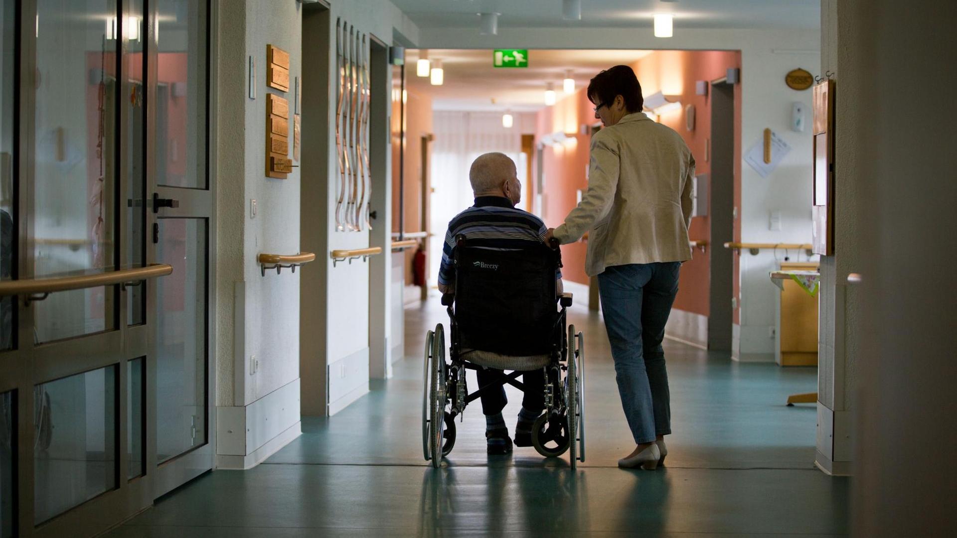 Eine Frau mit einem Mann in einem Rollstuhl in einem Gang eines Pflegeheims. Eine Frau mit einem Mann in einem Rollstuhl in einem Gang eines Pflegeheims.