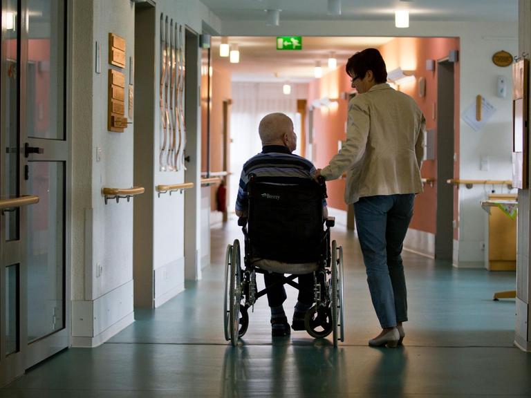 Eine Frau mit einem Mann in einem Rollstuhl in einem Gang eines Pflegeheims.