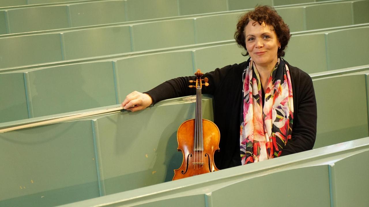 Die Musikerin sitzt inmitten der leeren Kirchenbänke mit ihrer Bratsche und lächelt. Die Musikerin sitzt inmitten der leeren Kirchenbänke mit ihrer Bratsche und lächelt.
