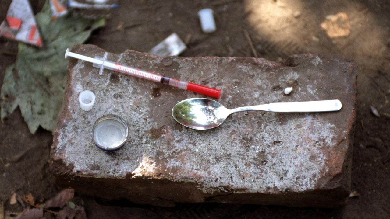 Auf einem Stein im Park liegen Utensilien für den Heroinkonsum: Ein Teelöfel und eine Spritze.