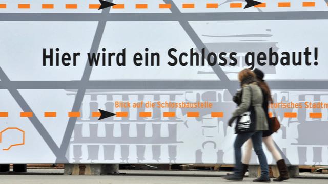 Zwei Frauen gehen in Berlin in der Straße Unter den Linden an dem Grundstück vorbei, auf dem das Stadtschloss errichtet werden soll.