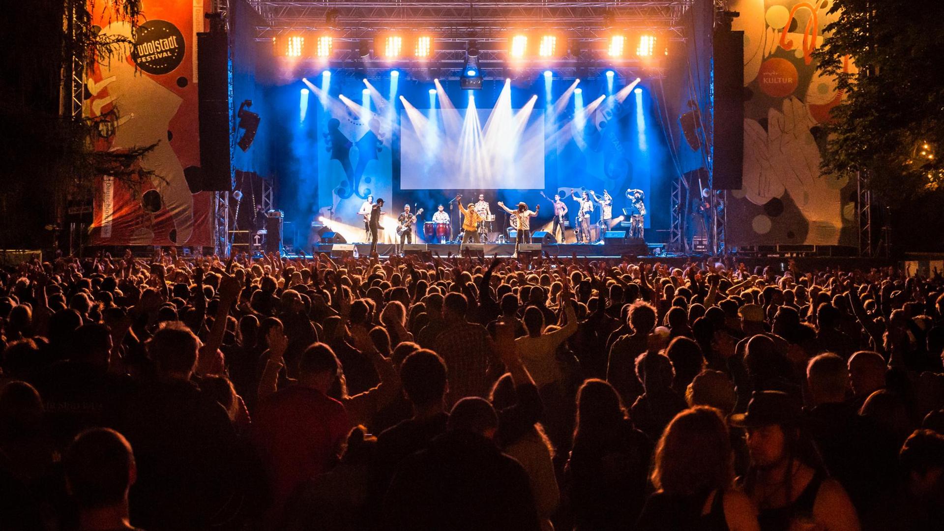 Nachtaufnahme eines Konzerts in Rudolstadt, im Vordergrund ist das Puiblikum zu sehen, im Hintergrund die hell erleuchtete Bühne mit Musikern. Nachtaufnahme eines Konzerts in Rudolstadt, im Vordergrund ist das Puiblikum zu sehen, im Hintergrund die hell erleuchtete Bühne mit Musikern.
