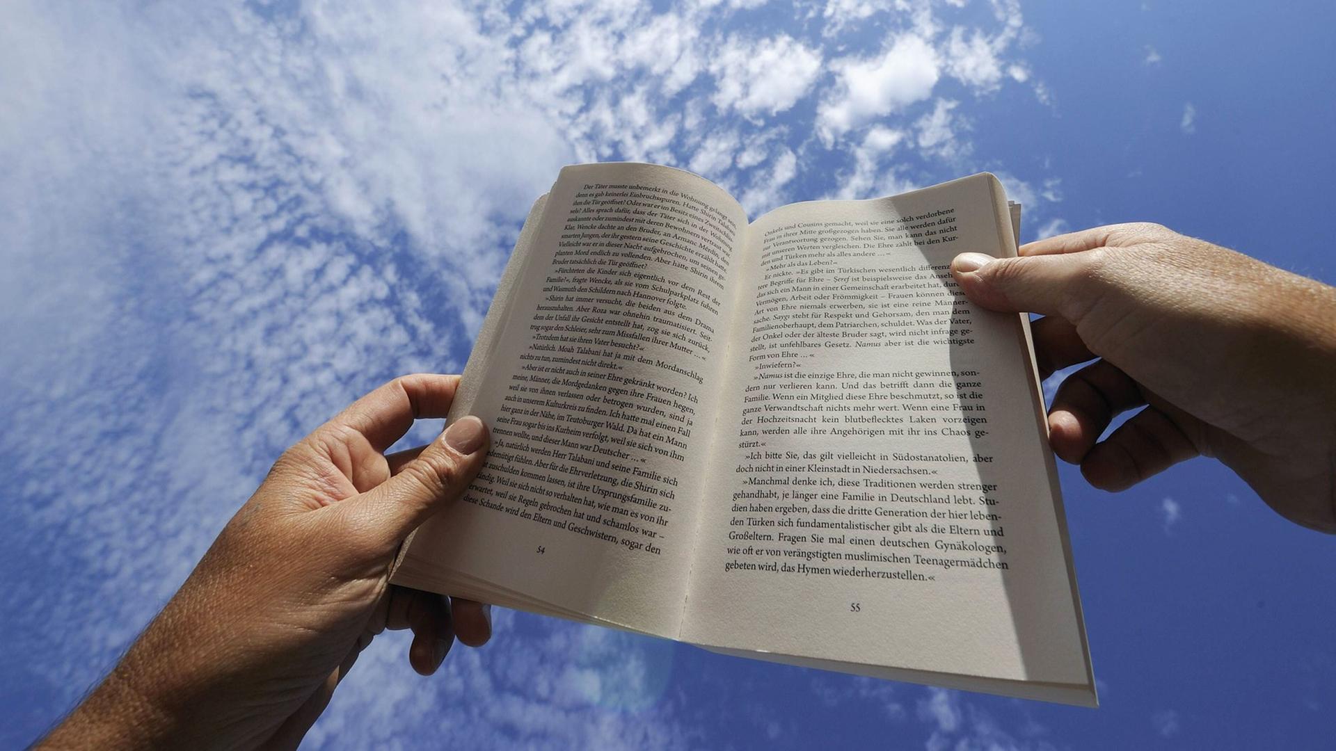 Zwei Hände halten ein Buch vor strahlend blauem Himmel. Zwei Hände halten ein Buch vor strahlend blauem Himmel.