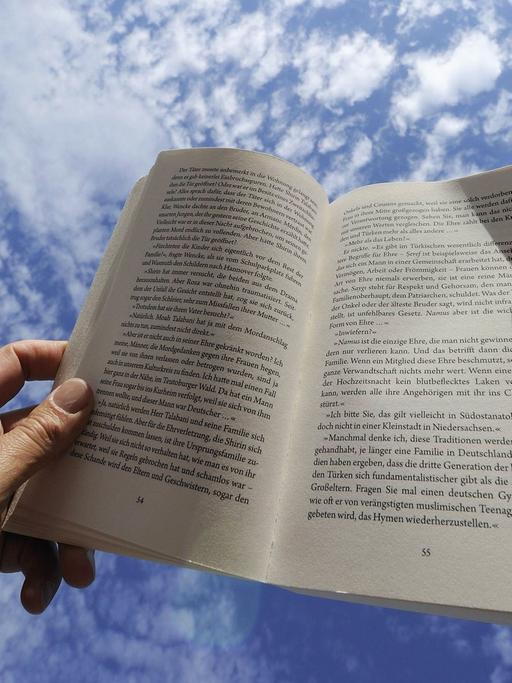 Zwei Hände halten ein Buch vor strahlend blauem Himmel.