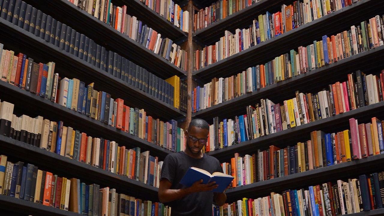 Ein Mann steht vor einem großen Bücherregal und liest.