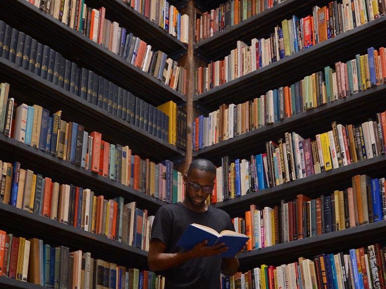 Ein Mann steht vor einem großen Bücherregal und liest.