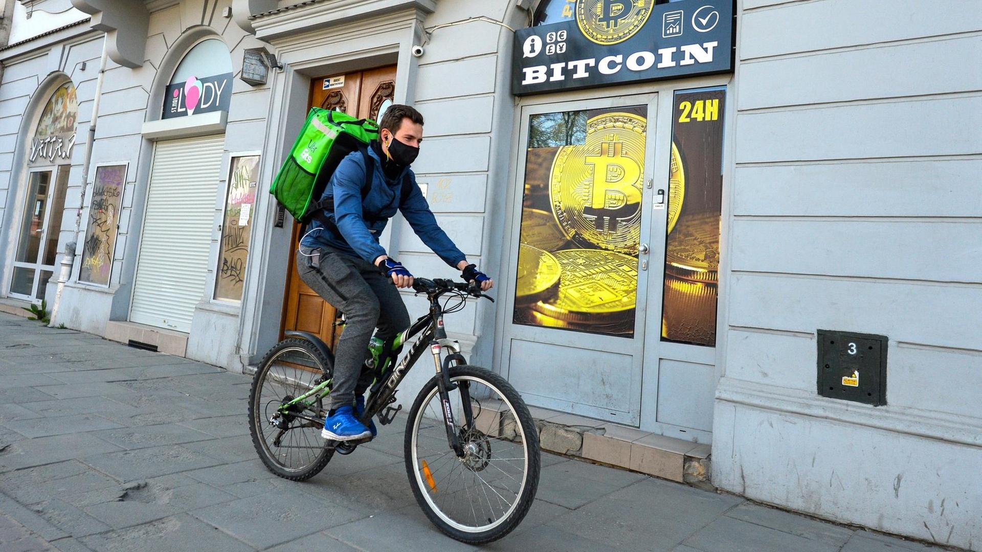 Ein Radfahrer mit Mundschutz fährt an einem Bitcoin-Wechsel-Laden in Krakau vorbei.