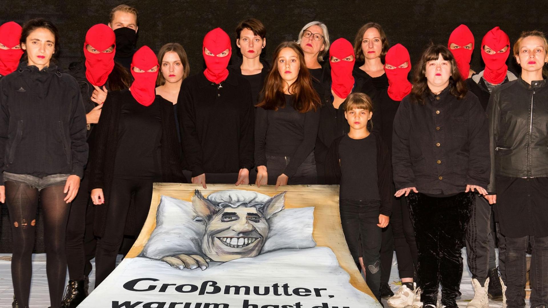 Eine Gruppe Menschen, zum Teil mit roten Sturmmasken vermummt, stehen hinter einem Transparent. Eine Gruppe Menschen, zum Teil mit roten Sturmmasken vermummt, stehen hinter einem Transparent.