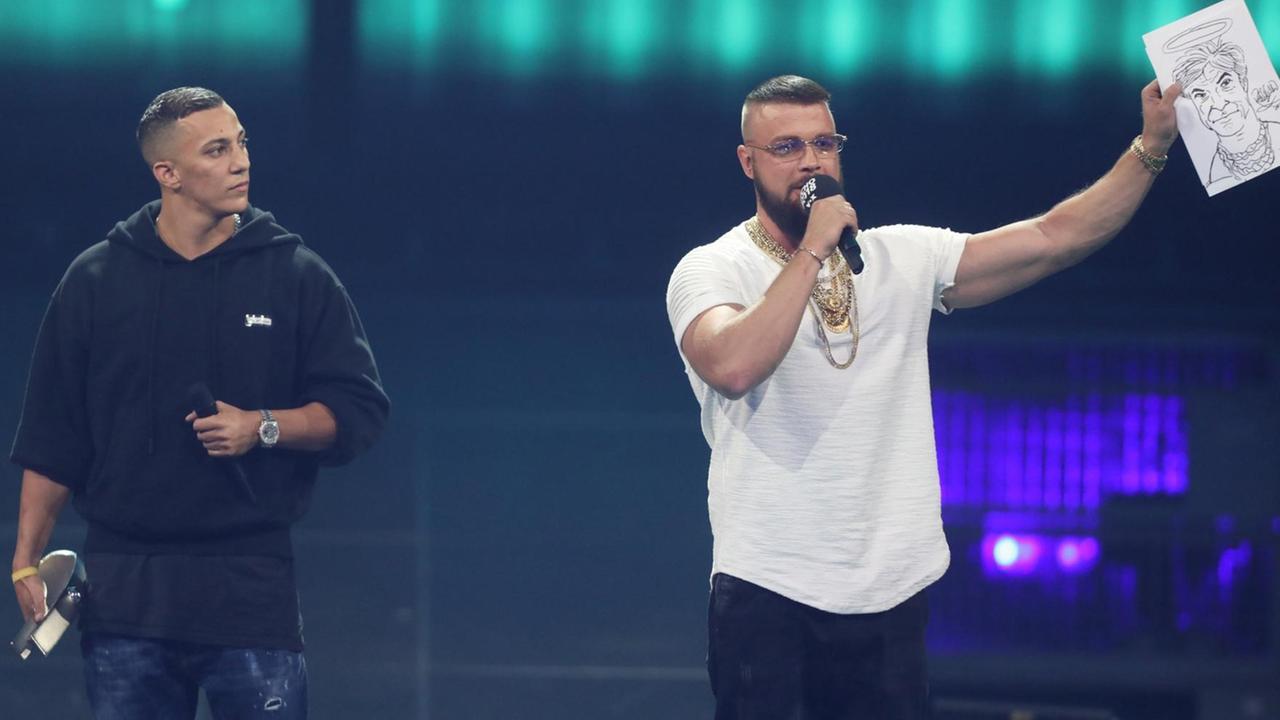 12.04.2018, Berlin: Kollegah (r) und Farid Bang erhalten den Echo für Album des Jahres bei der 27. Verleihung des Deutschen Musikpreises Echo. Die Rapper halten eine Karrikatur von Sänger Campino mit Heiligenschein hoch, welches sie versteigern wollen. Foto: Jörg Carstensen/dpa | Verwendung weltweit 12.04.2018, Berlin: Kollegah (r) und Farid Bang erhalten den Echo für Album des Jahres bei der 27. Verleihung des Deutschen Musikpreises Echo. Die Rapper halten eine Karrikatur von Sänger Campino mit Heiligenschein hoch, welches sie versteigern wollen. Foto: Jörg Carstensen/dpa | Verwendung weltweit