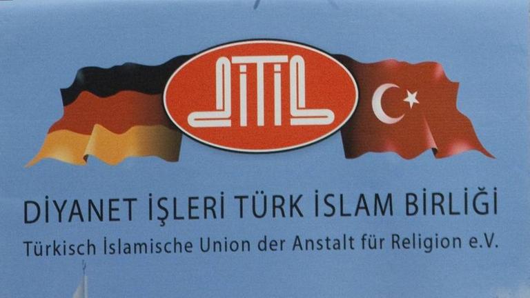 Ausschnitt aus einem Poster, dass eine Deutschlandflagge und eine Türkeiflagge zeigt, dazwischen der Schriftzug Ditib. Darunter steht der vollständige Name des Vereins zuerst groß auf Türkisch, dann klein auf Deutsch. 
