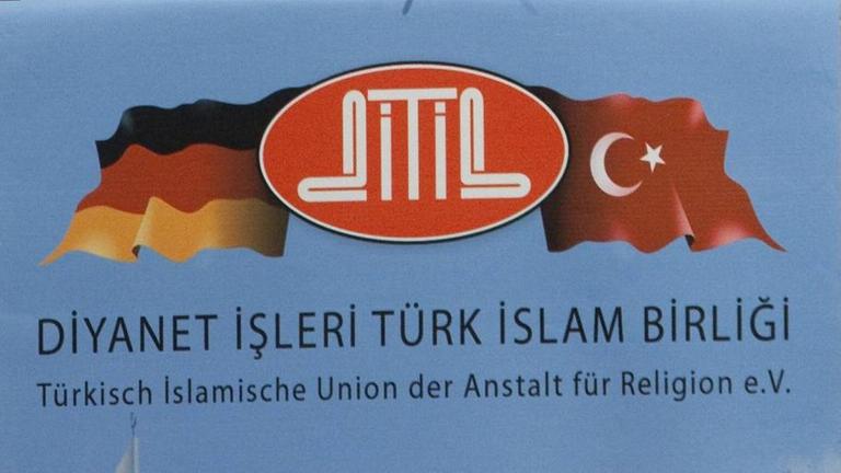 Ausschnitt aus einem Poster, dass eine Deutschlandflagge und eine Türkeiflagge zeigt, dazwischen der Schriftzug Ditib. Darunter steht der vollständige Name des Vereins zuerst groß auf Türkisch, dann klein auf Deutsch. Ausschnitt aus einem Poster, dass eine Deutschlandflagge und eine Türkeiflagge zeigt, dazwischen der Schriftzug Ditib. Darunter steht der vollständige Name des Vereins zuerst groß auf Türkisch, dann klein auf Deutsch.