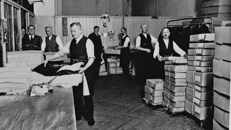 Eines der wenigen verbliebenen Fotos, das die Innenräume des Berliner Modeunternehmens von Leopold Seligmann zeigt (1930): Mehrere elegant gekleidete Angestellte packen Kleidungsstücke in Kisten und Kartons.