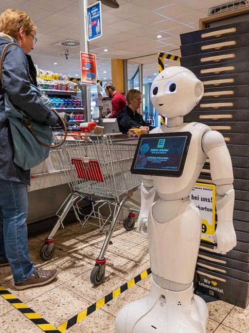 In Nordrhein-Westfalen steht der Pflegeroboter «Pepper» im Kassenbereich des Supermarktes und weist Kunden darauf hin, Abstand zu halten.